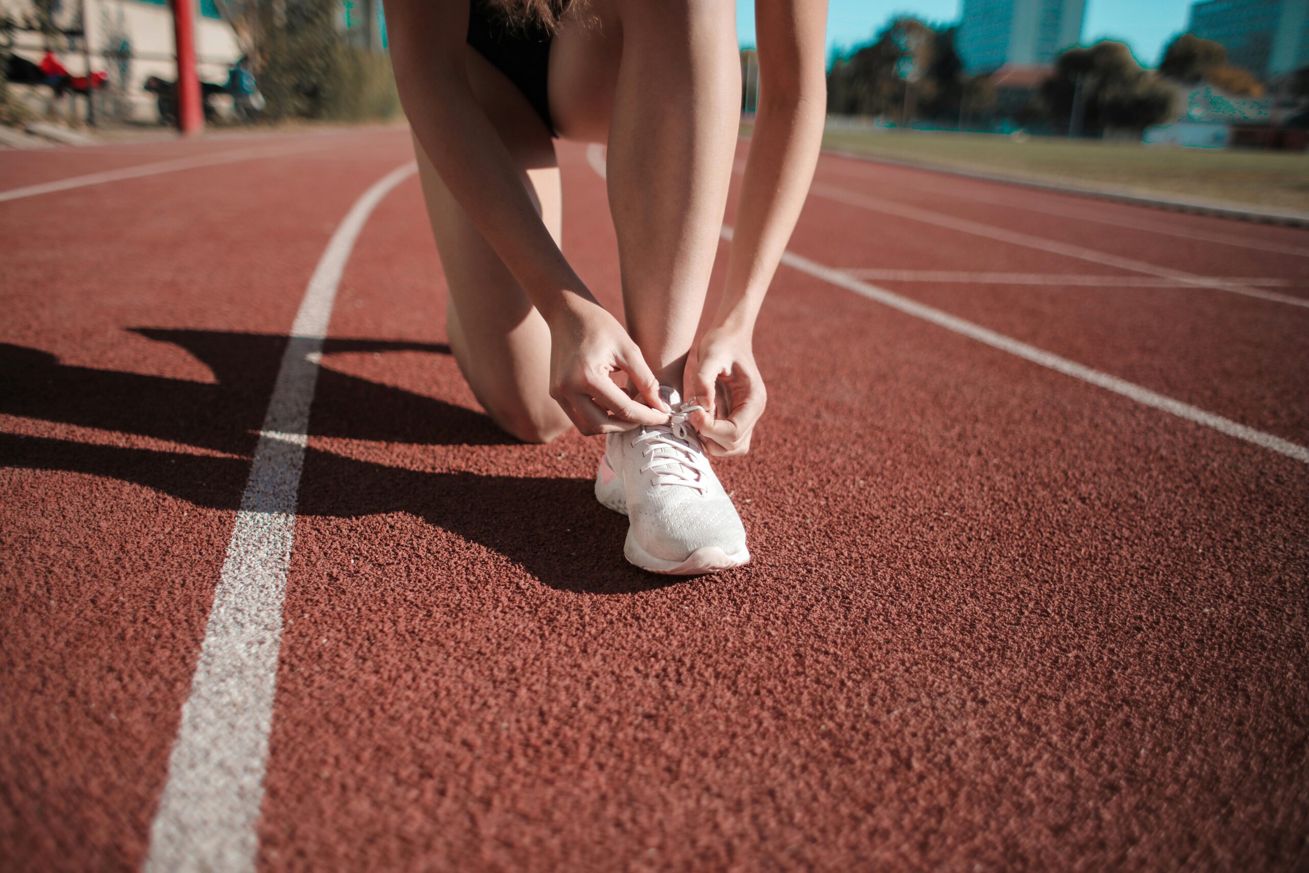 Palestinian Runner Sara Ali Sets New Record at London Marathon, Dedicates Victory to Gaza. Close-up of a woman tying her shoes on a running track, ready to sprint.